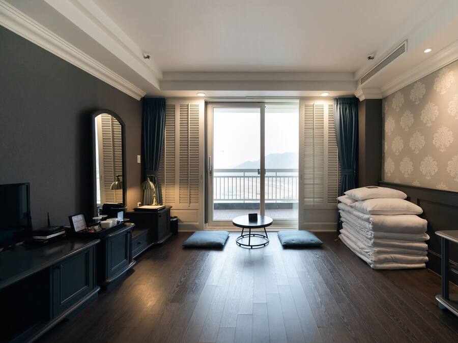 A hotel room with a balcony, a desk with a chair, a bed with pillows, and a TV.