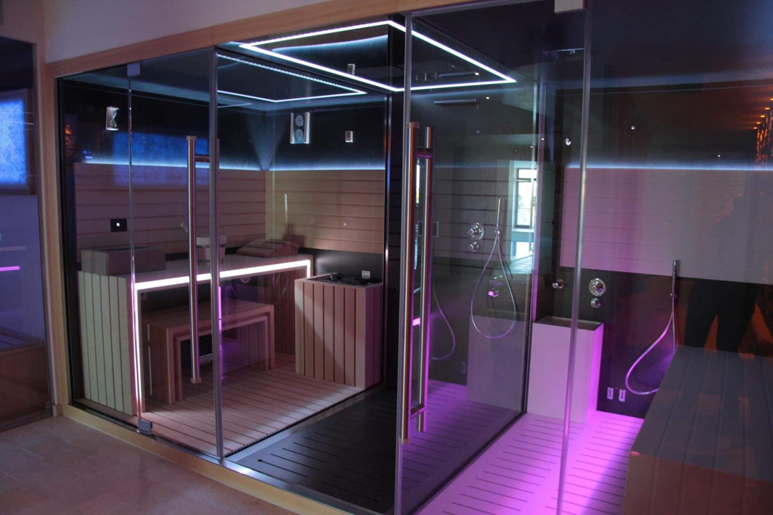 A modern, glass-walled room with a wooden floor, a small seating area, and a visible shower area.