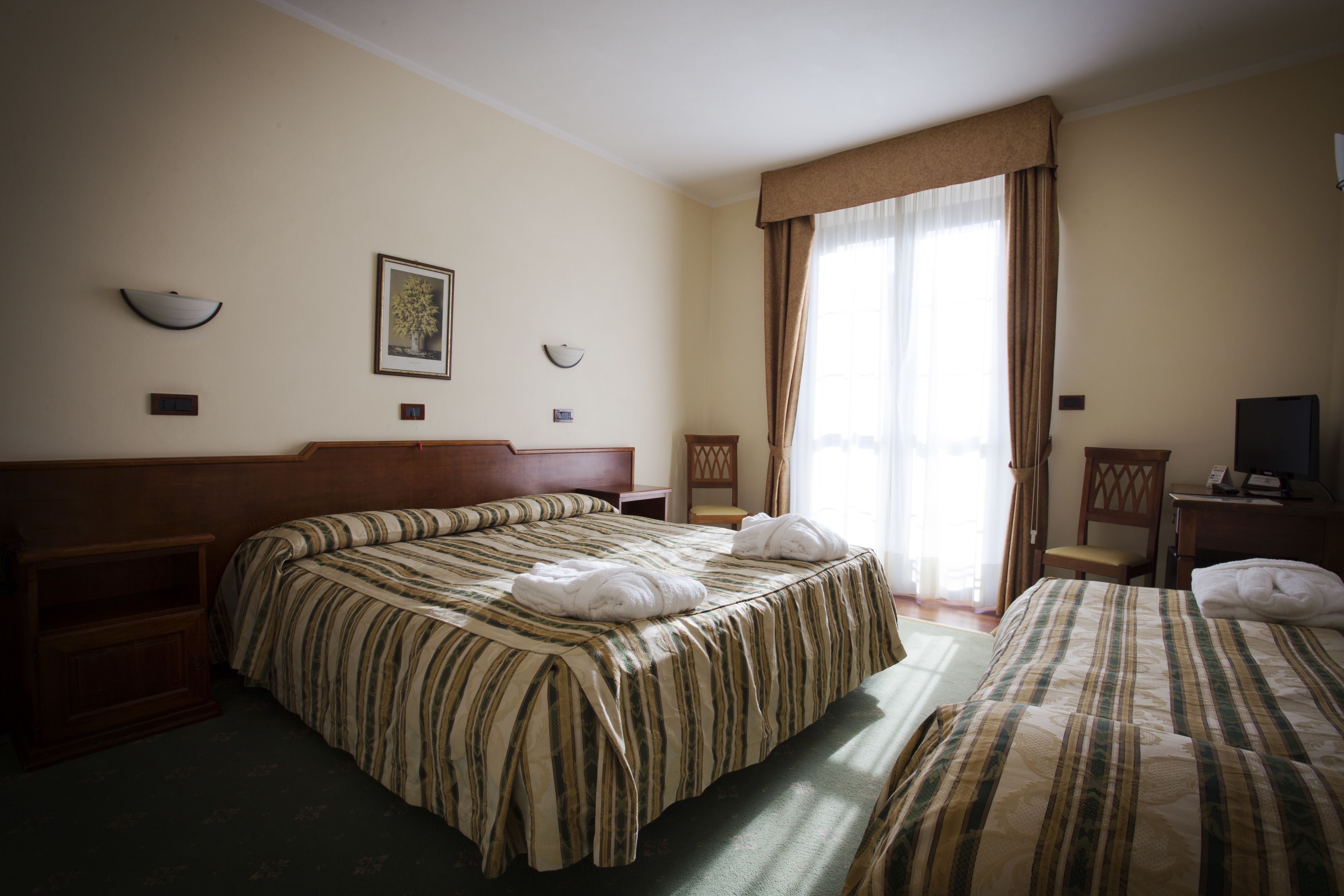 Una habitación de hotel con dos camas, un cabecero de madera, un escritorio con una silla y un televisor.