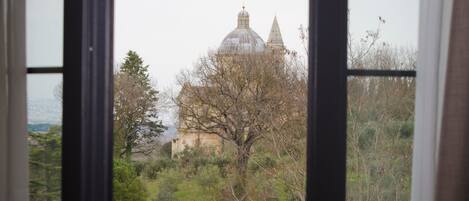 A view through a window with a metal railing, featuring a building with a dome and trees in the background.