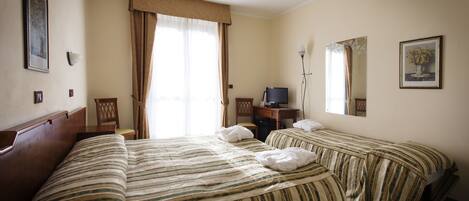 Habitación de hotel con dos camas, un escritorio, una silla, un televisor y una ventana con cortinas.