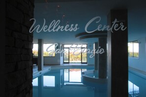 Centro de bienestar con una amplia piscina interior, grandes ventanales y una pared de piedra.