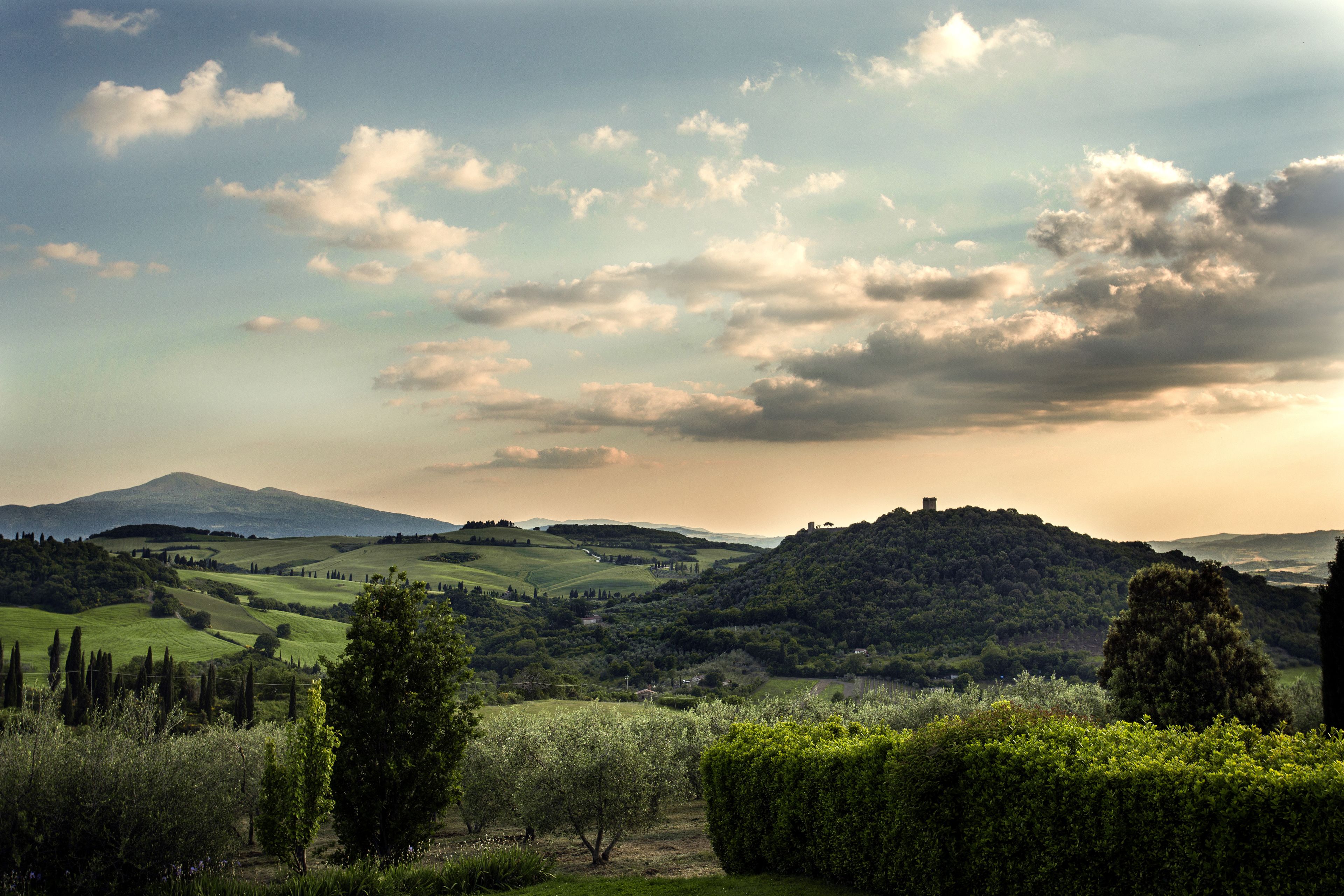 Paesaggio suggestivo con dolci colline, una montagna sullo sfondo e cielo sereno.