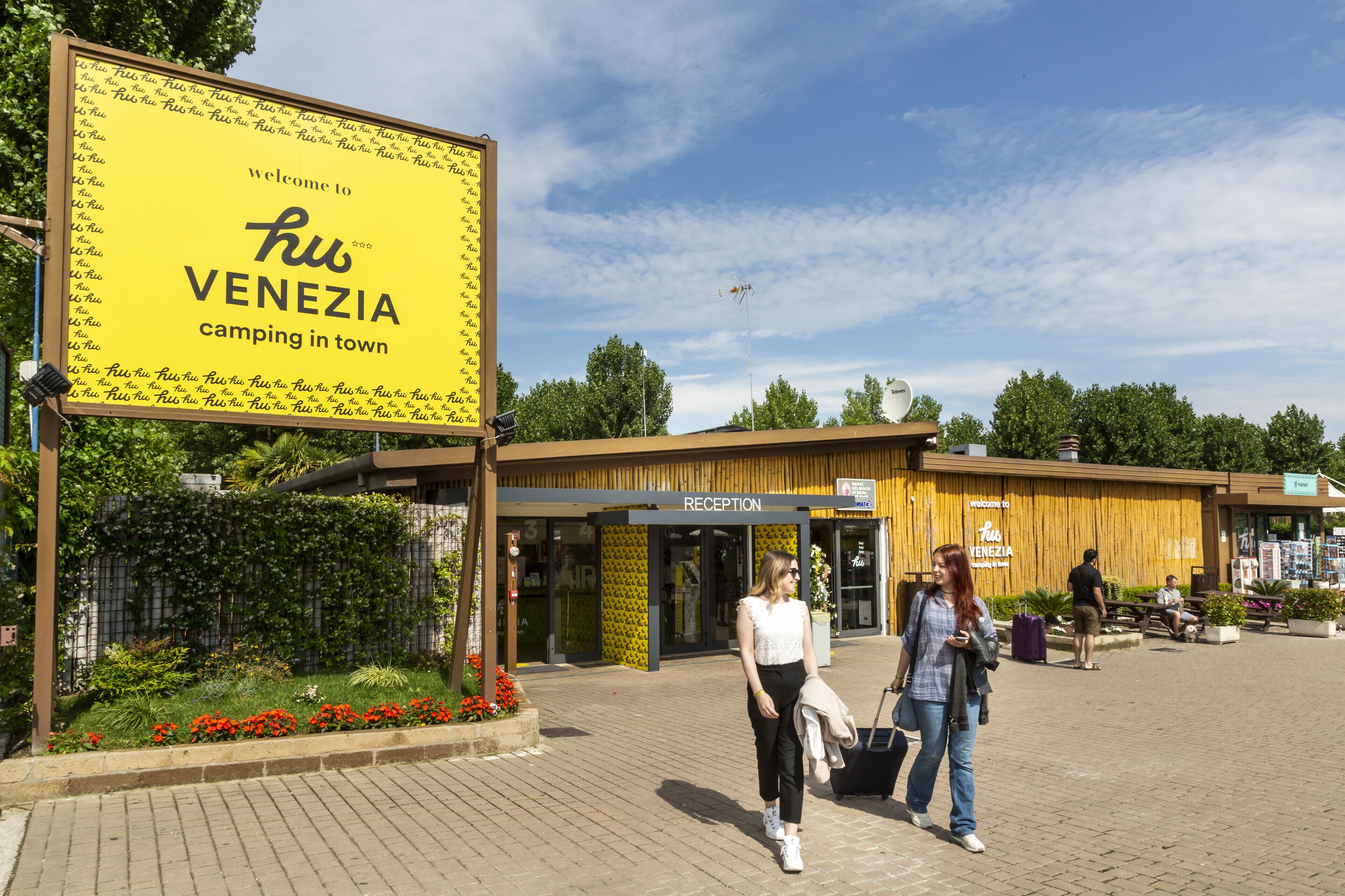 Une pancarte accueillant les visiteurs au camping « ku VENEZIA », situé en ville, avec un espace de réception en arrière-plan.