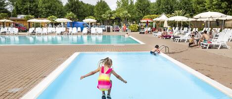 A swimming pool with lounge chairs and umbrellas, surrounded by trees.