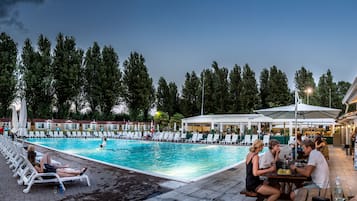 A swimming pool area with lounge chairs and umbrellas, surrounded by trees and buildings.