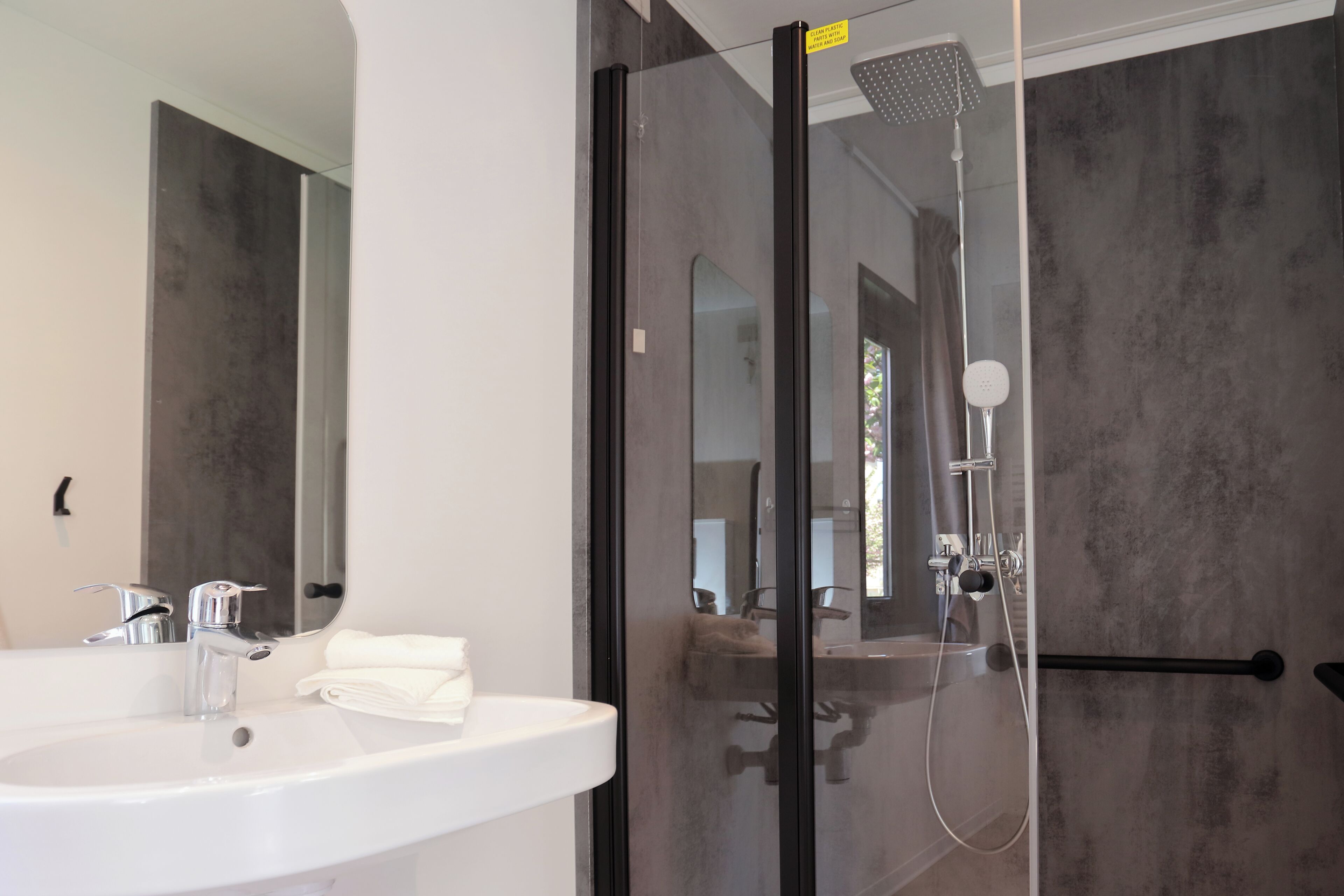 Ein modernes Badezimmer mit einem weißen Waschbecken, einer Duschkabine aus Glas und einem großen Spiegel.