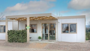 Ein modernes eingeschossiges Haus mit einer überdachten Veranda, einem Eingang mit Glastür und einem kleinen Garten.