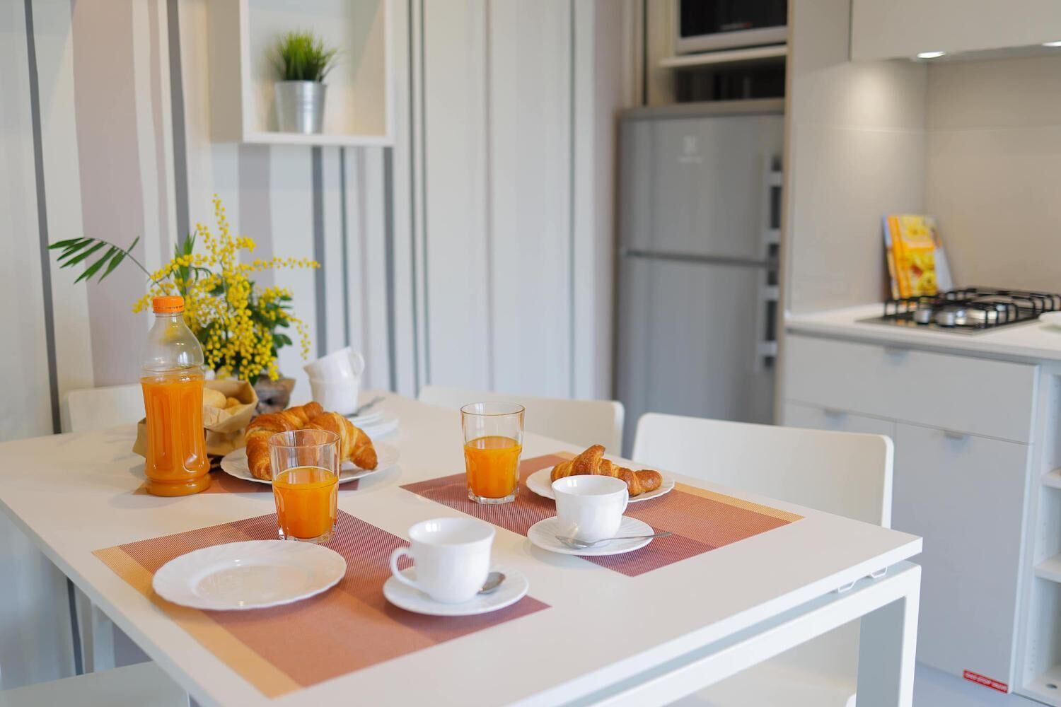 A breakfast setup with croissants, orange juice, and coffee on a table in a modern kitchen.