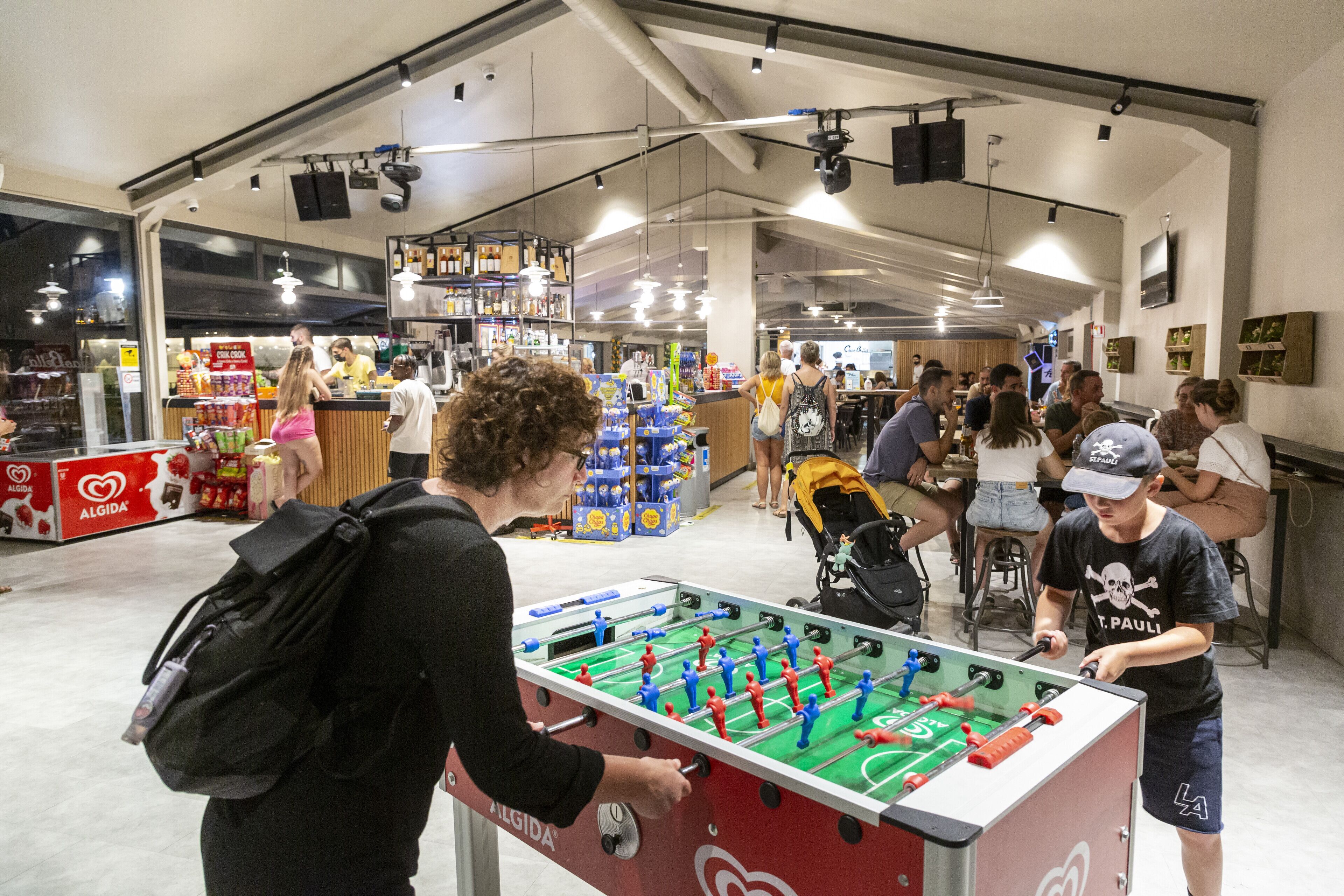 A spacious indoor area with a foosball table, seating, and a variety of food and drink options.