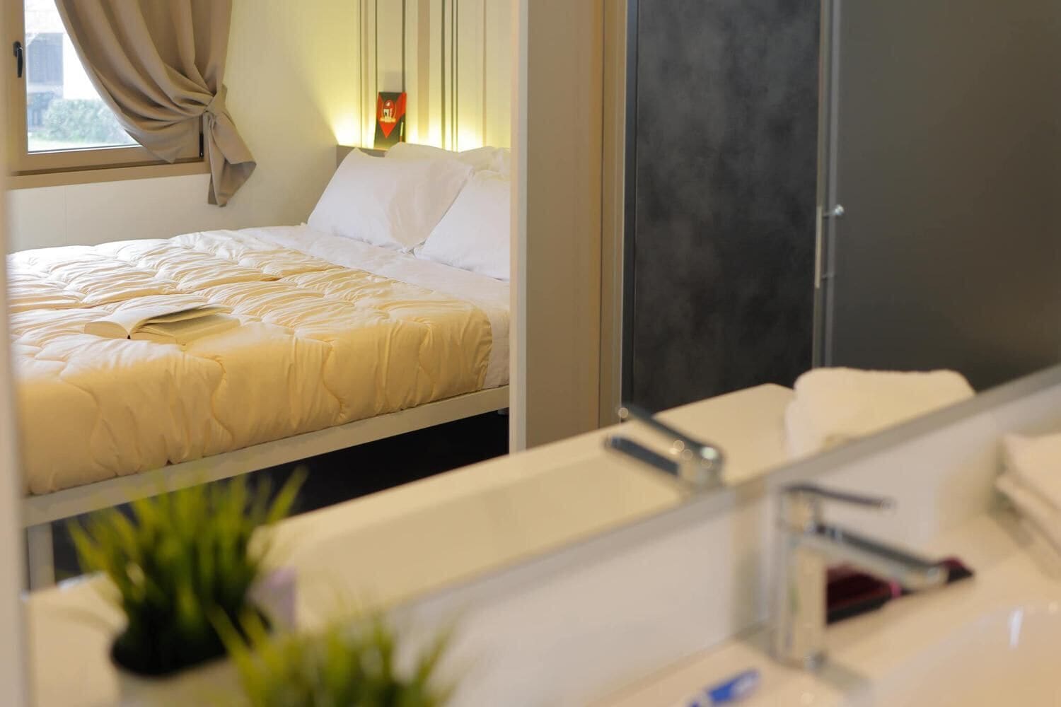 Ein modernes Hotelzimmer mit einem Bett, einem großen Spiegel und einem Badezimmer mit Waschbecken und einer Pflanze.