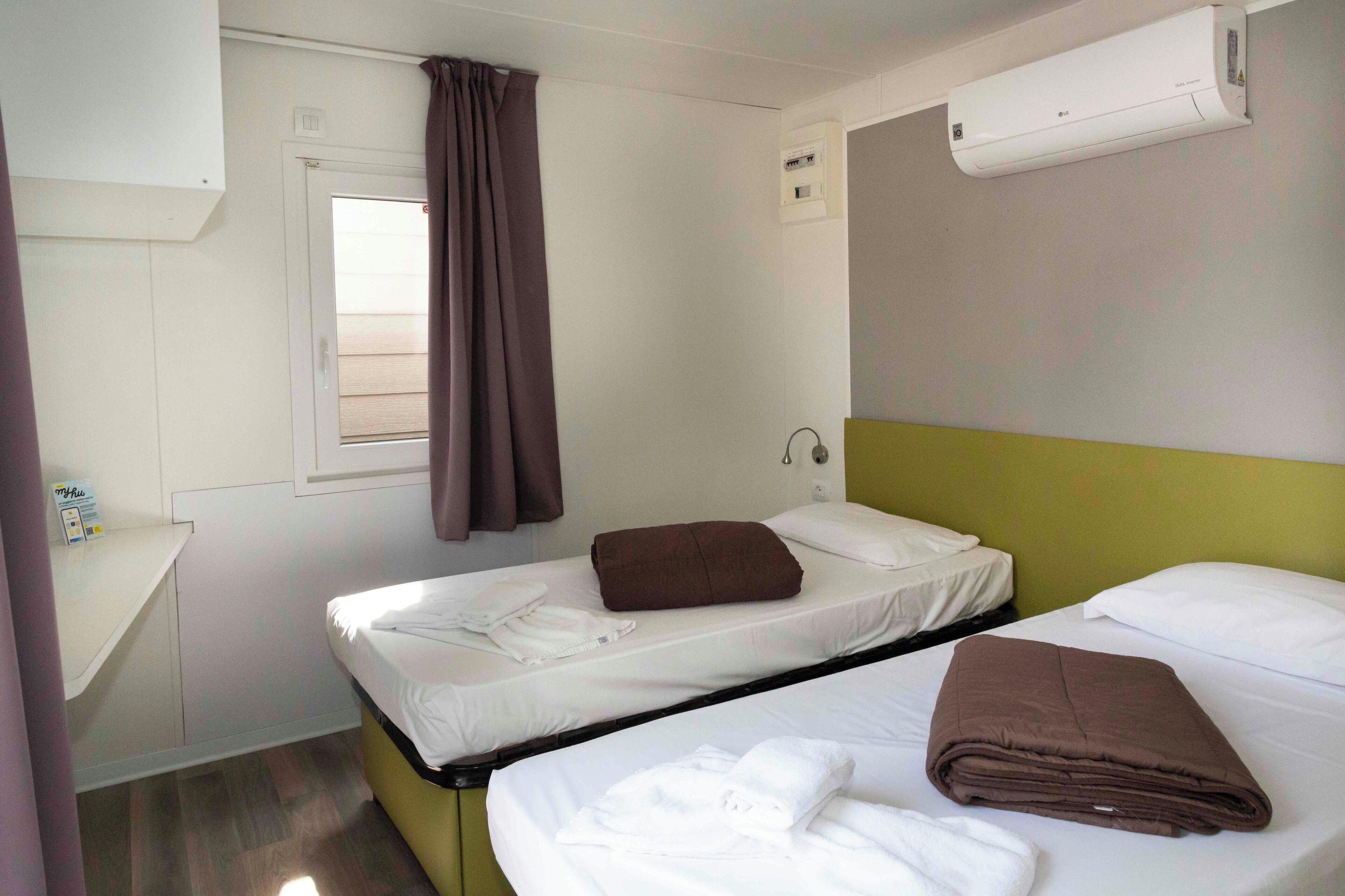 A hotel room with two beds, a desk, and an air conditioning unit.