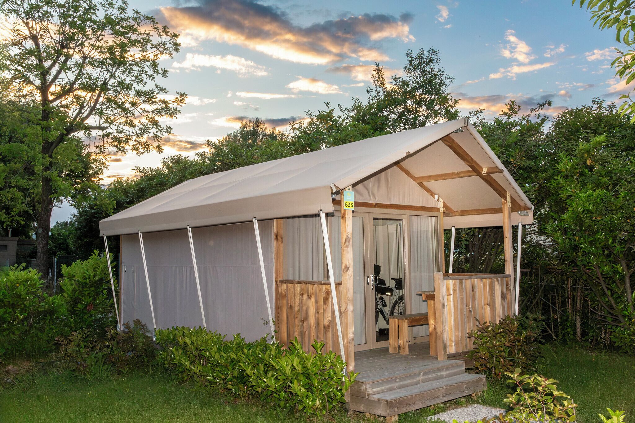 Une petite tente à un seul niveau, dotée d’une terrasse en bois et contenant un vélo à l’intérieur.