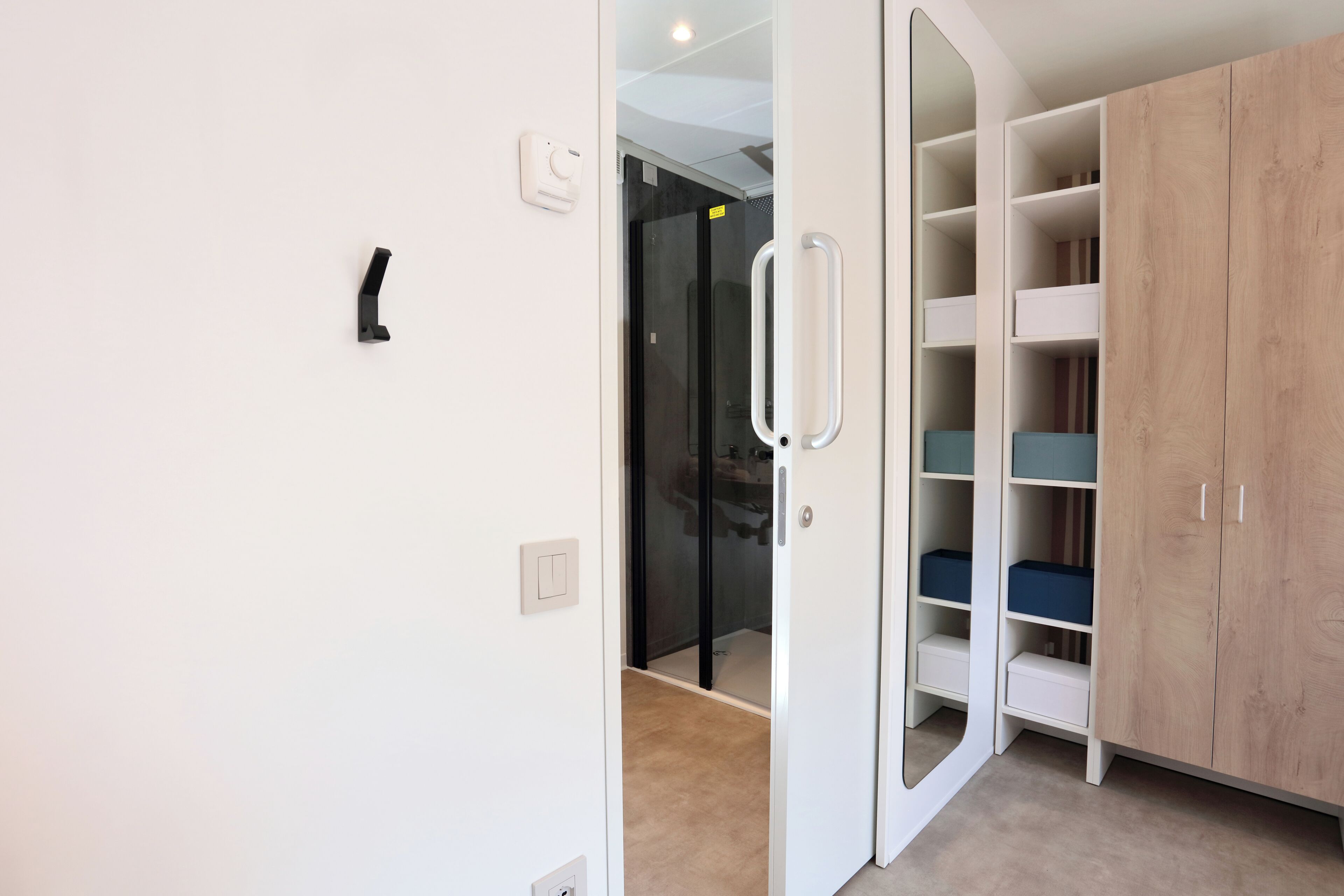 Une pièce avec une armoire blanche, une porte en verre et un tapis beige.