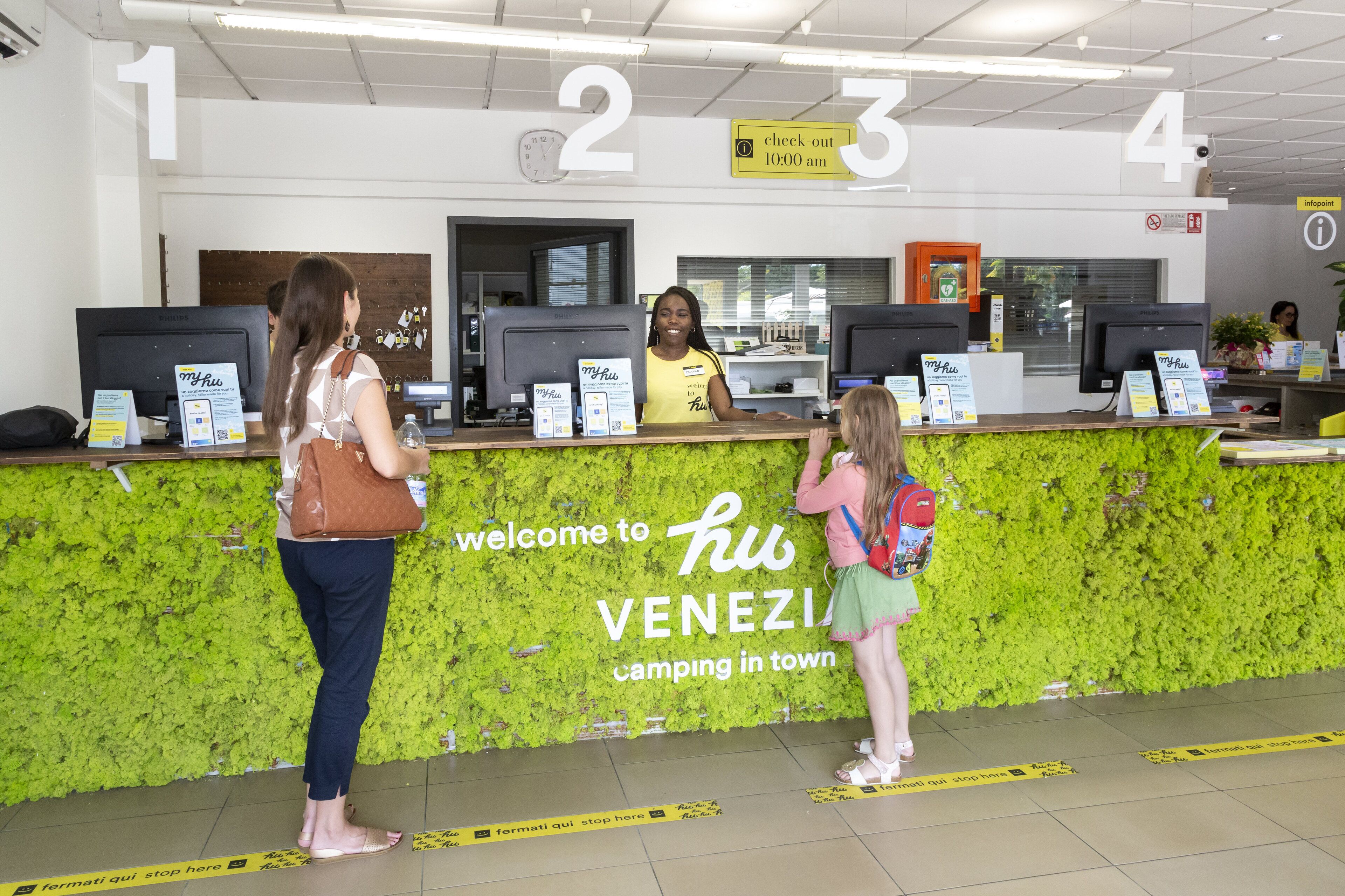 Un comptoir d’accueil avec un mur vert et une enseigne sur laquelle on peut lire : « Bienvenue au camping hu VENEZIA, en ville. »