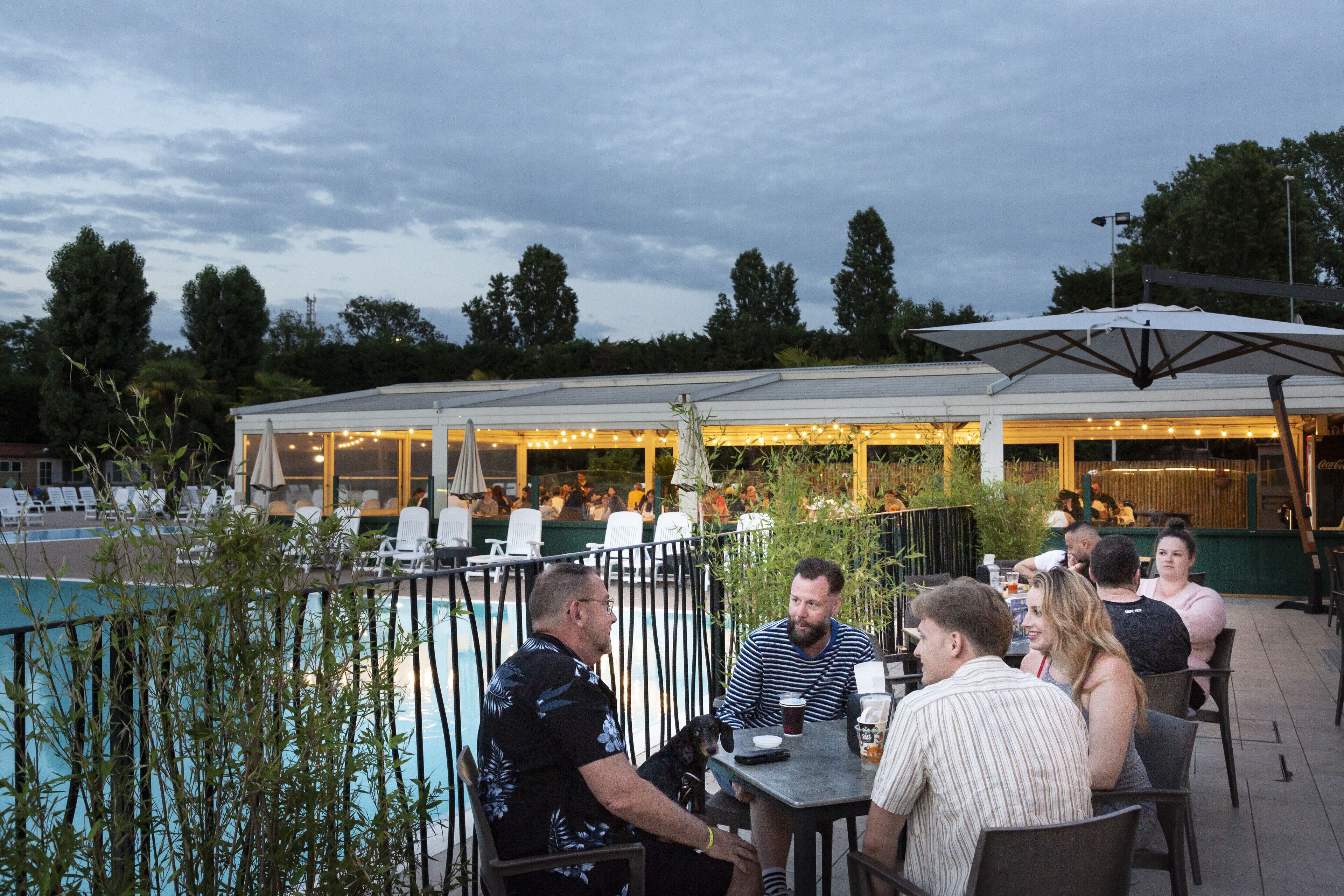 An outdoor dining area with tables and chairs, a pool, and a covered seating area with string lights.