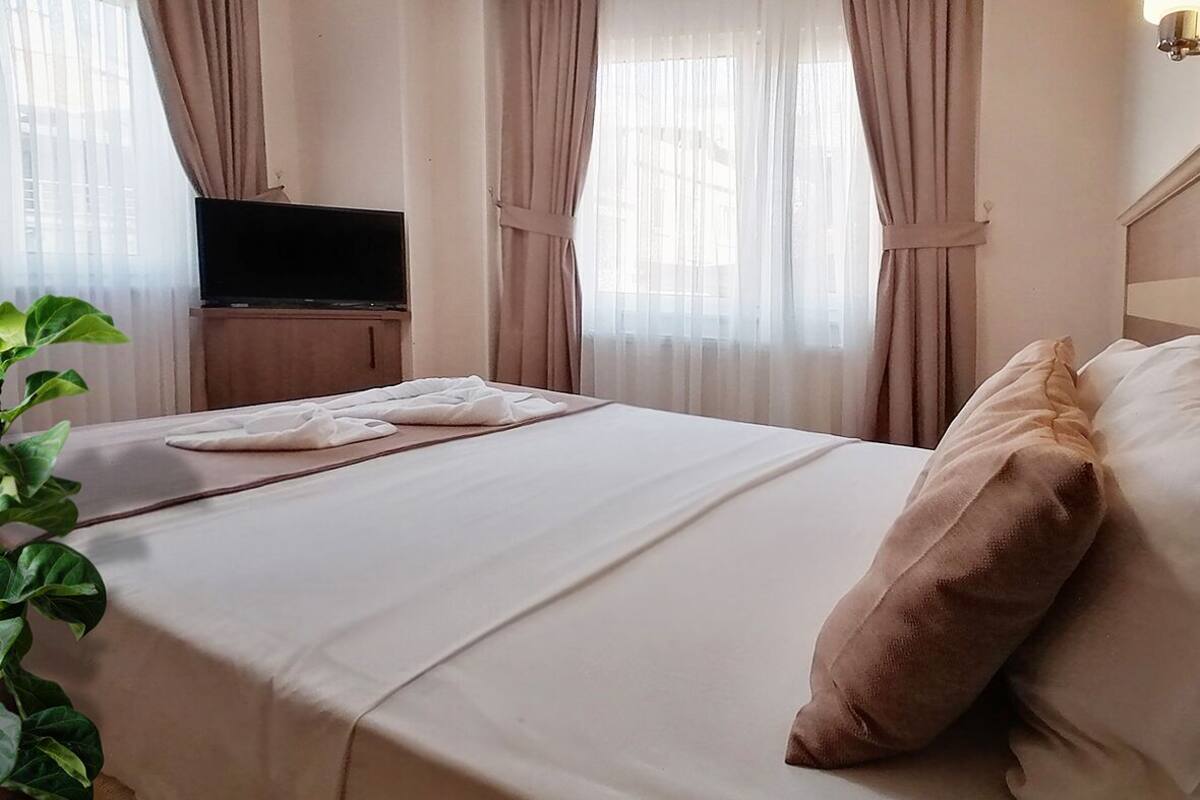 A hotel room with a bed, a television on a wooden stand, and sheer curtains.