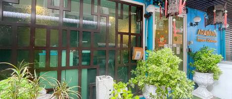 A storefront with a blue exterior, a large glass door, and various potted plants.