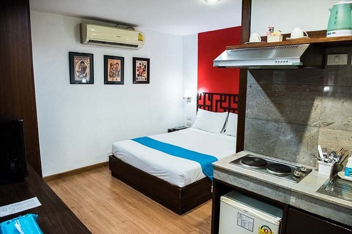 A compact hotel room with a bed, a kitchenette, and a wall-mounted air conditioner.