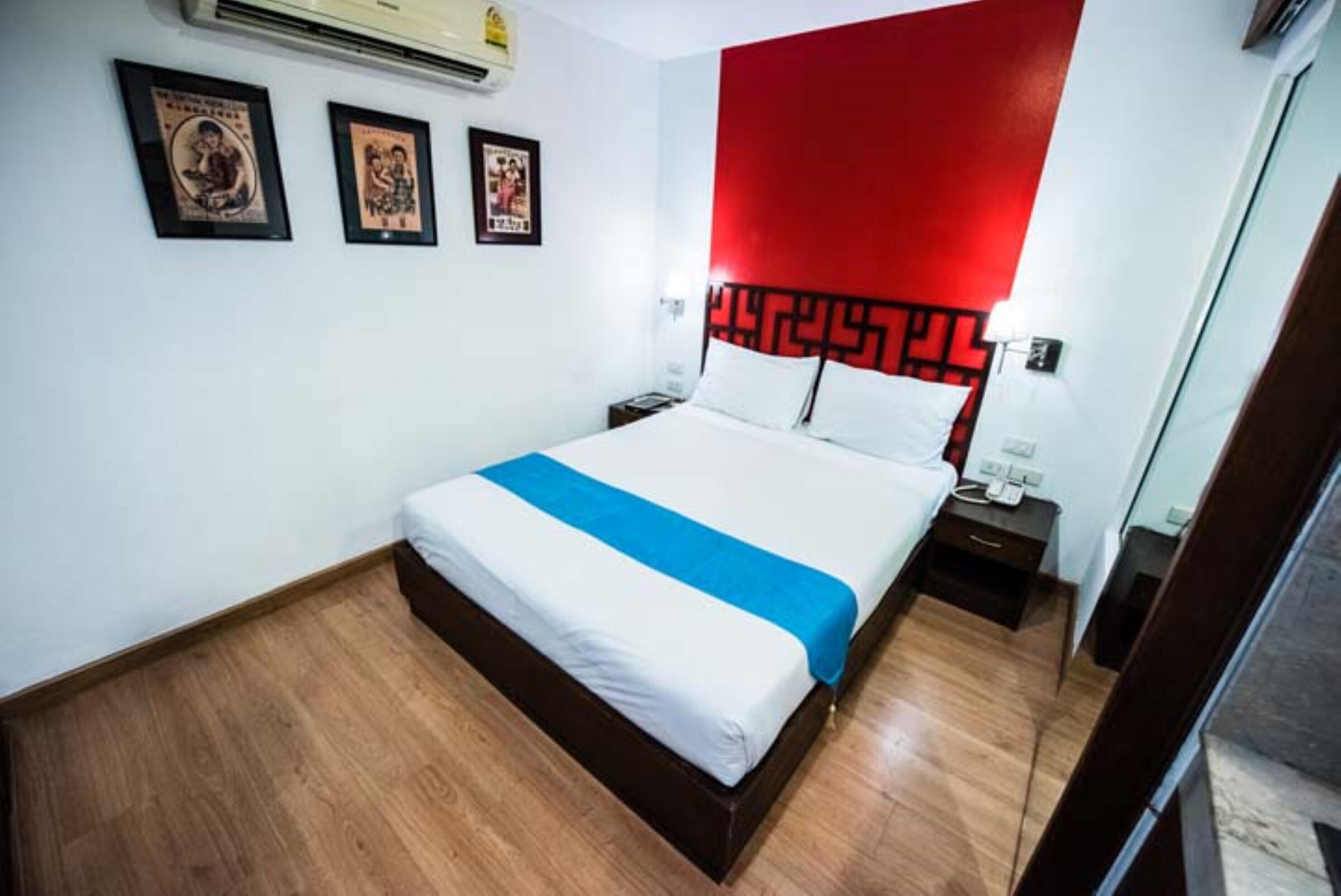 A hotel room with a bed, a nightstand, a red accent wall, and framed pictures on the wall.