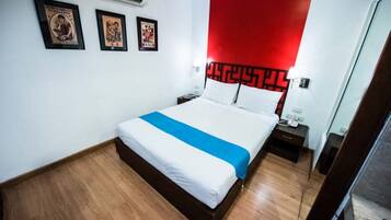 A hotel room with a bed, a nightstand, a red accent wall, and framed pictures on the wall.