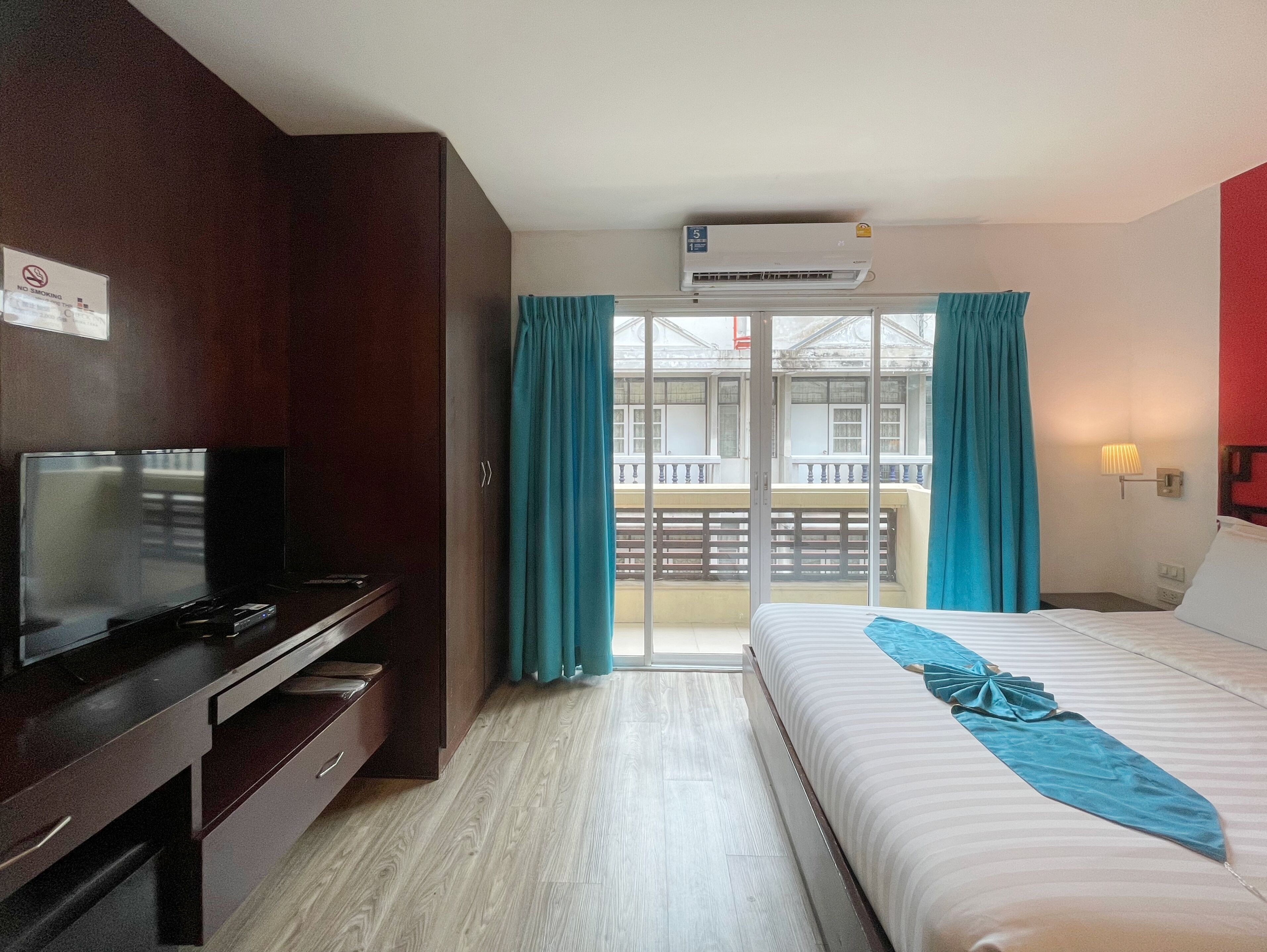 Habitación de hotel con cama, televisor, escritorio y balcón con cortinas.