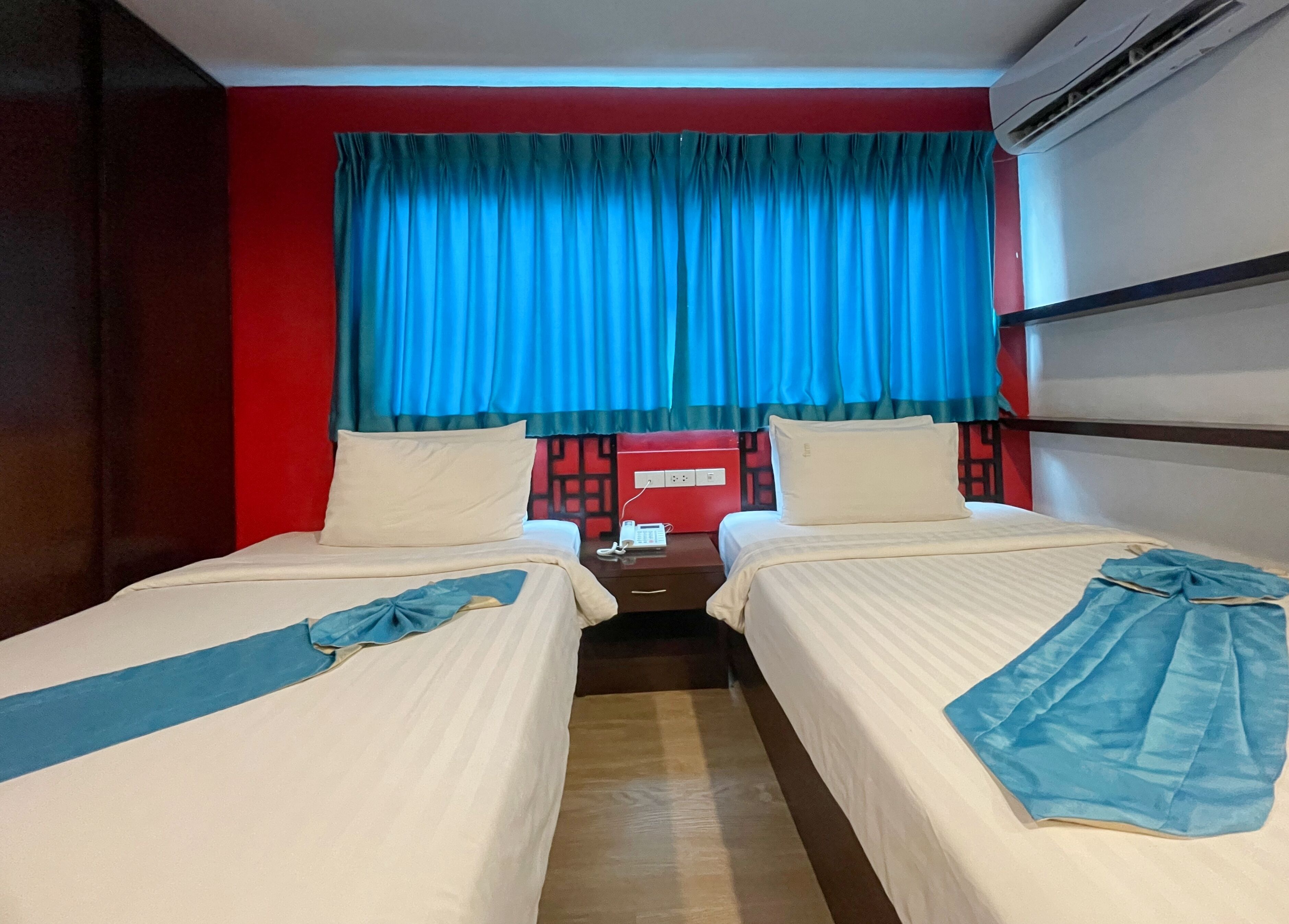 A hotel room with two beds, a red wall, a blue curtain, and an air conditioning unit.