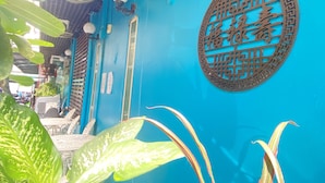 A blue building with a decorative metal emblem, outdoor seating, and potted plants. - Arawana Express Chinatown (Bangkok)