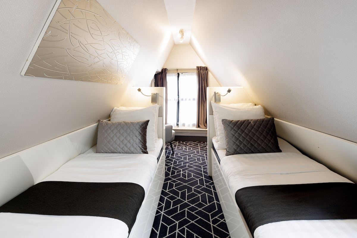 A compact room with two single beds, a central table, and a window with curtains.