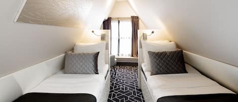 A compact room with two single beds, a central table, and a window with curtains.