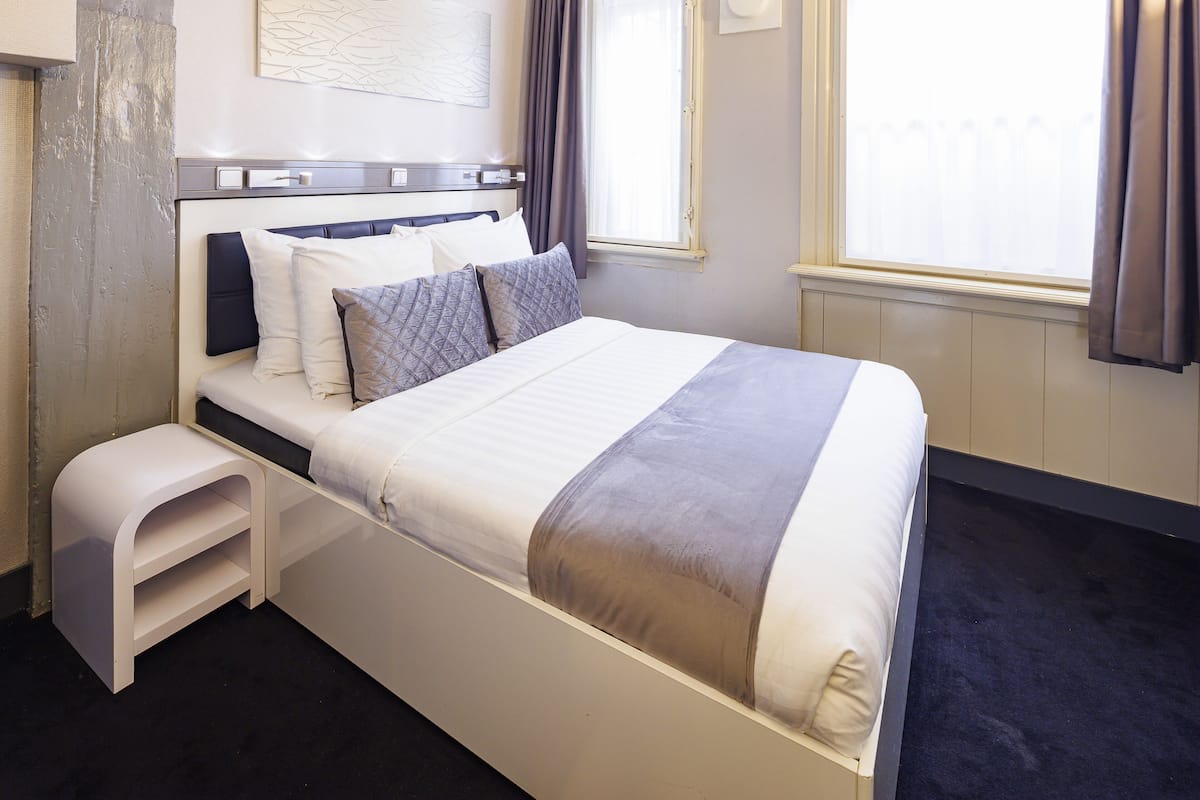 A neatly made bed with a headboard, a bedside table, and a window with curtains.