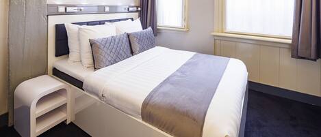 A neatly made bed with a headboard, a bedside table, and a window with curtains.