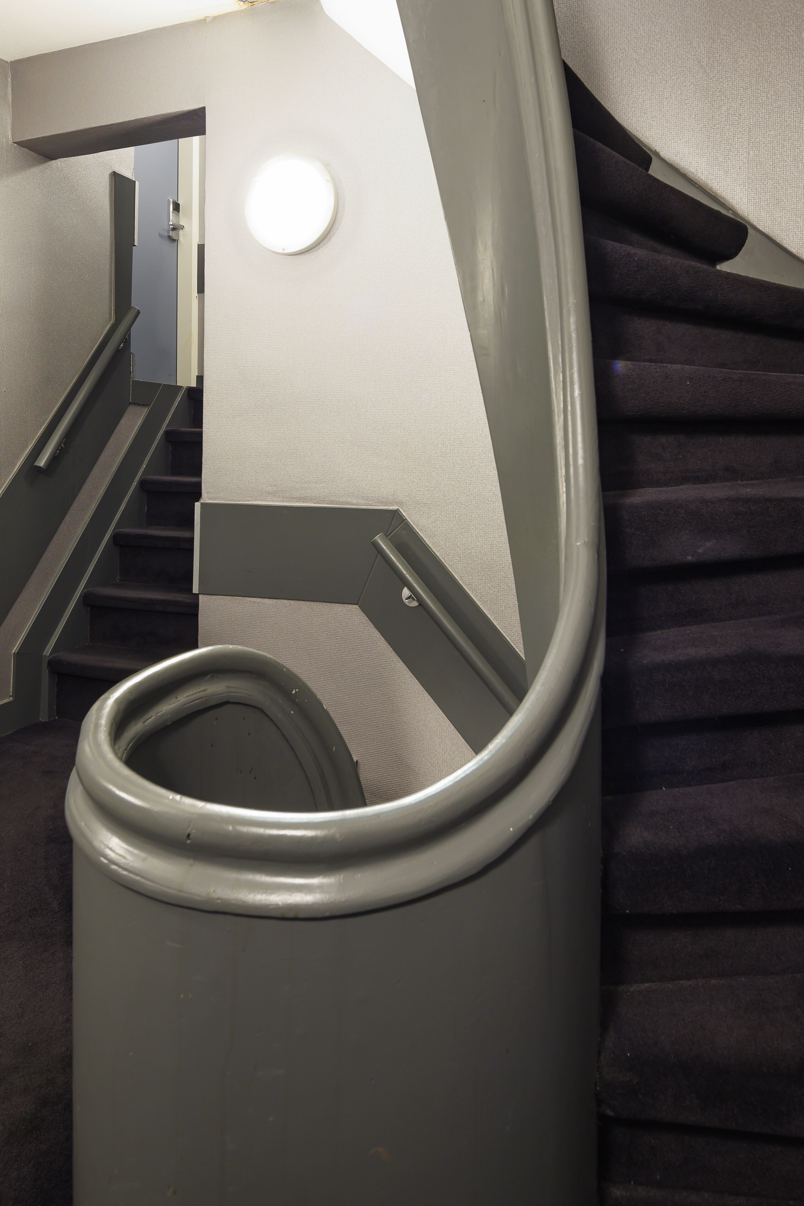 A staircase with a handrail and a circular light fixture on the wall.