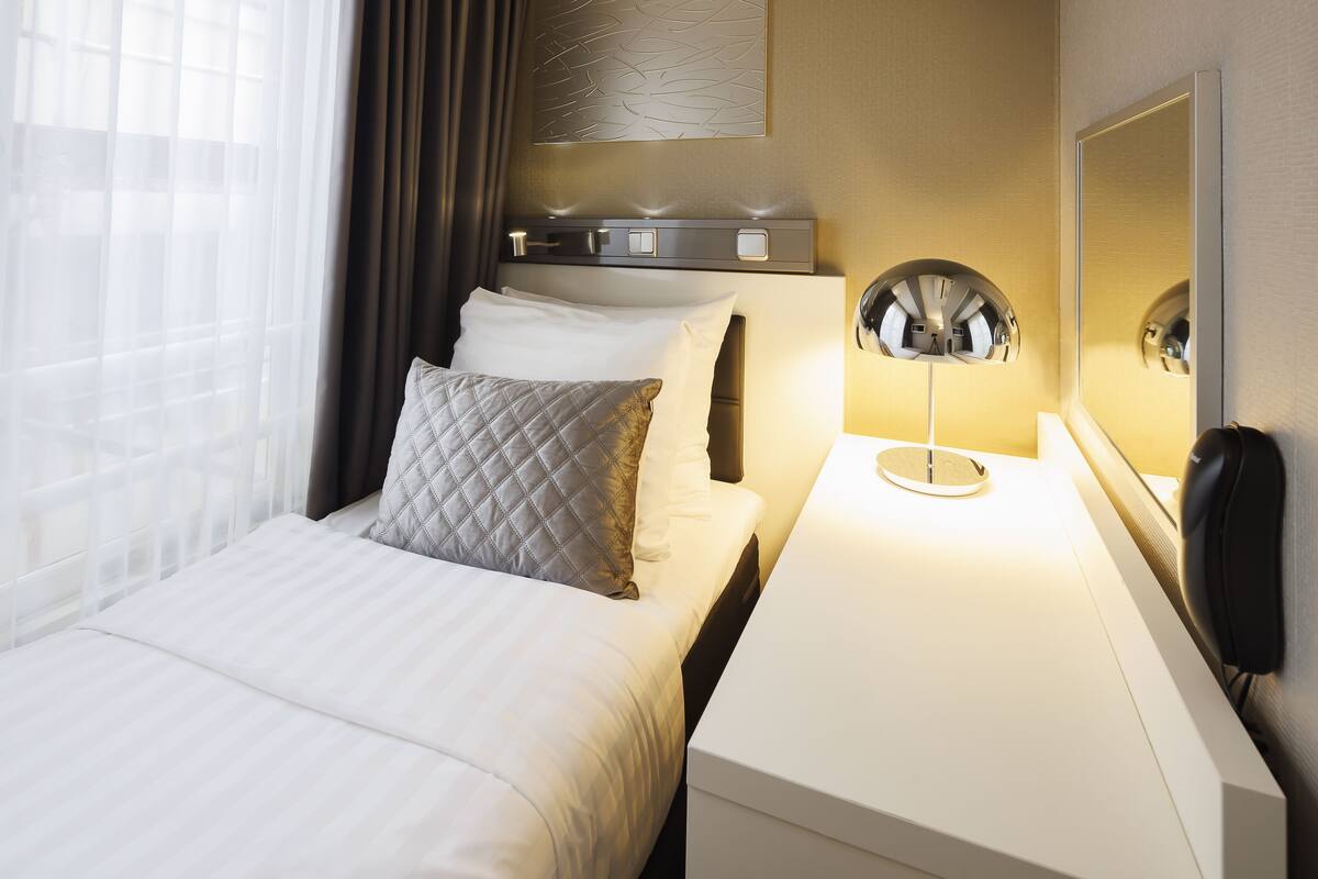 A hotel room with a bed, bedside table, lamp, and a mirror.