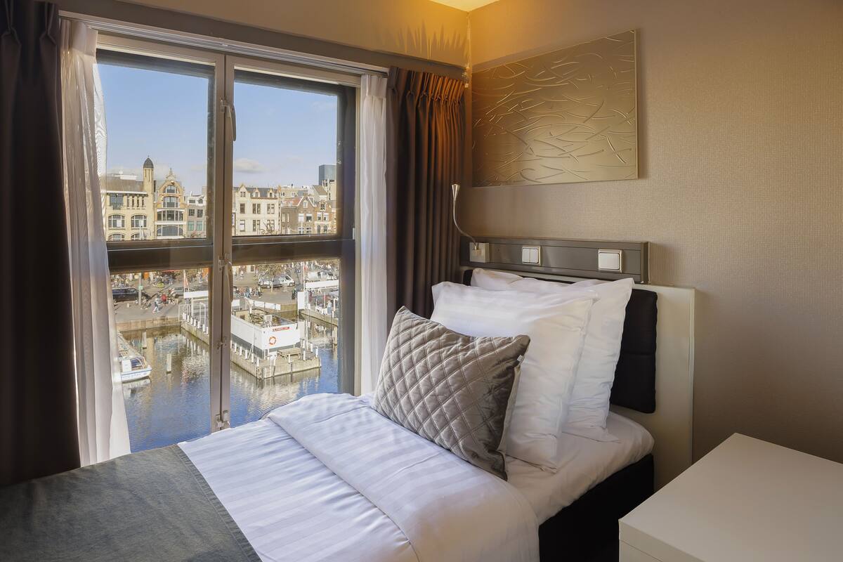 A hotel room with a bed, a view of a canal and buildings, and a modern wall design.