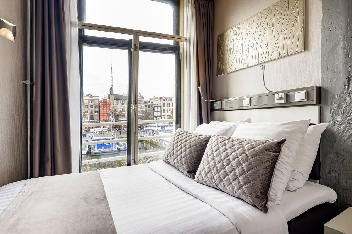 A hotel room with a large bed, a view of the cityscape through a window, and a modern wall design.