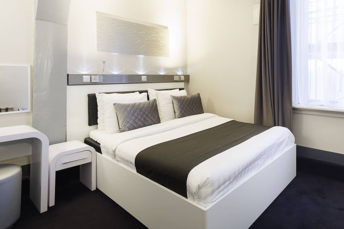 A modern hotel room with a neatly made bed, a small bedside table, and a window with curtains.