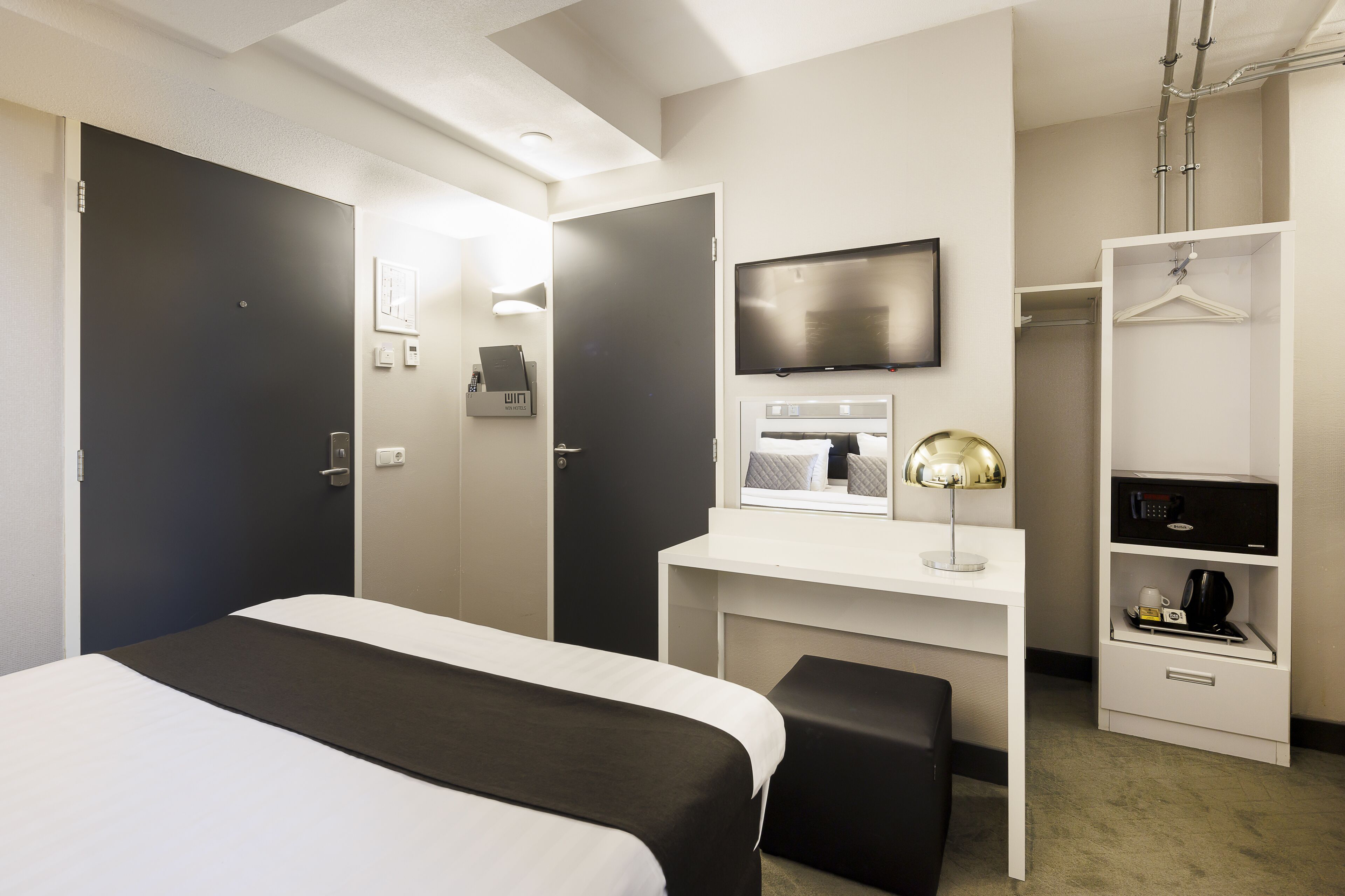A hotel room with a bed, a desk with a TV, a wardrobe, and a bedside table.