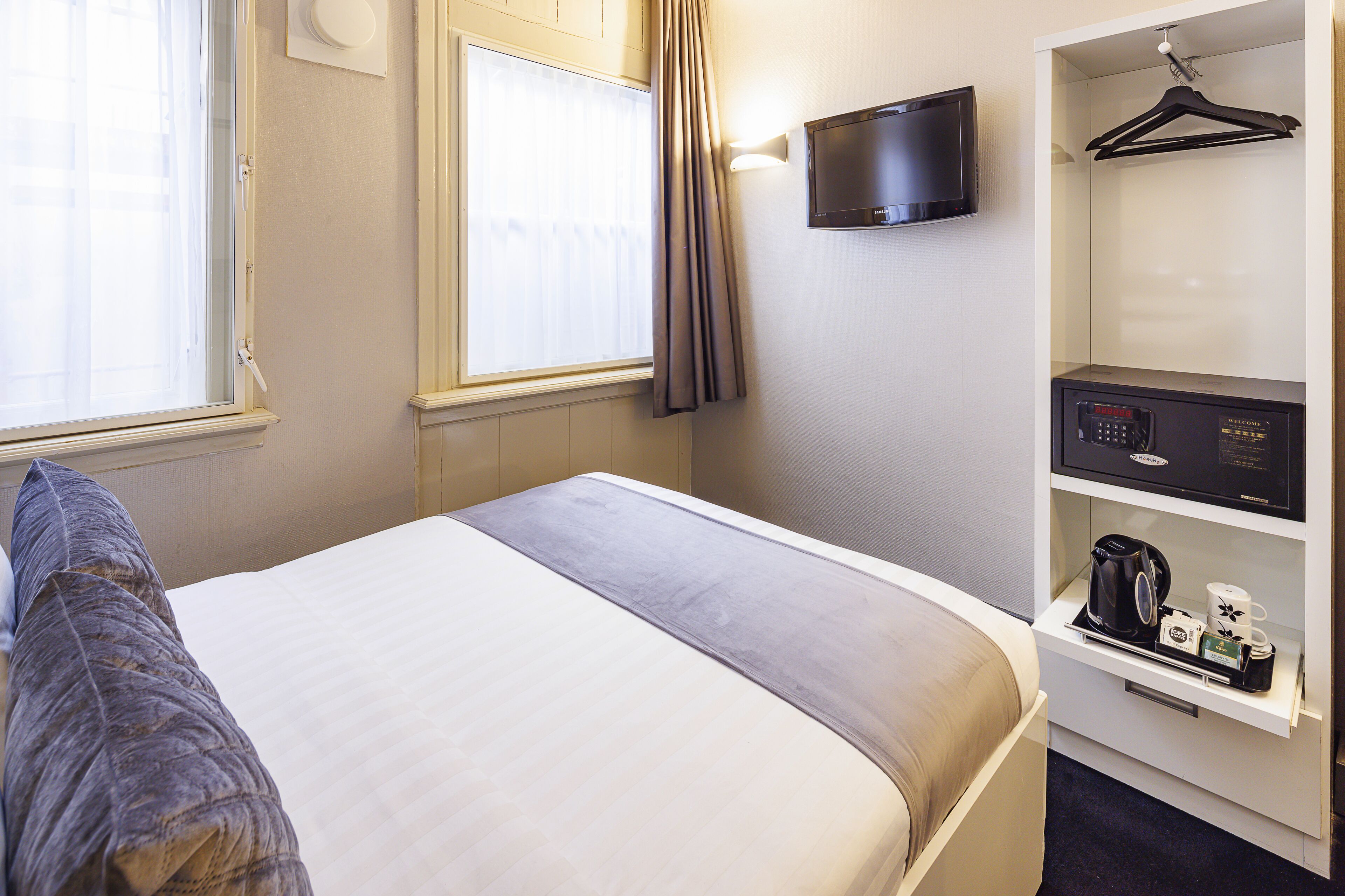 A hotel room with a bed, a TV mounted on the wall, a shelf with a coffee maker, and a hanging coat rack.
