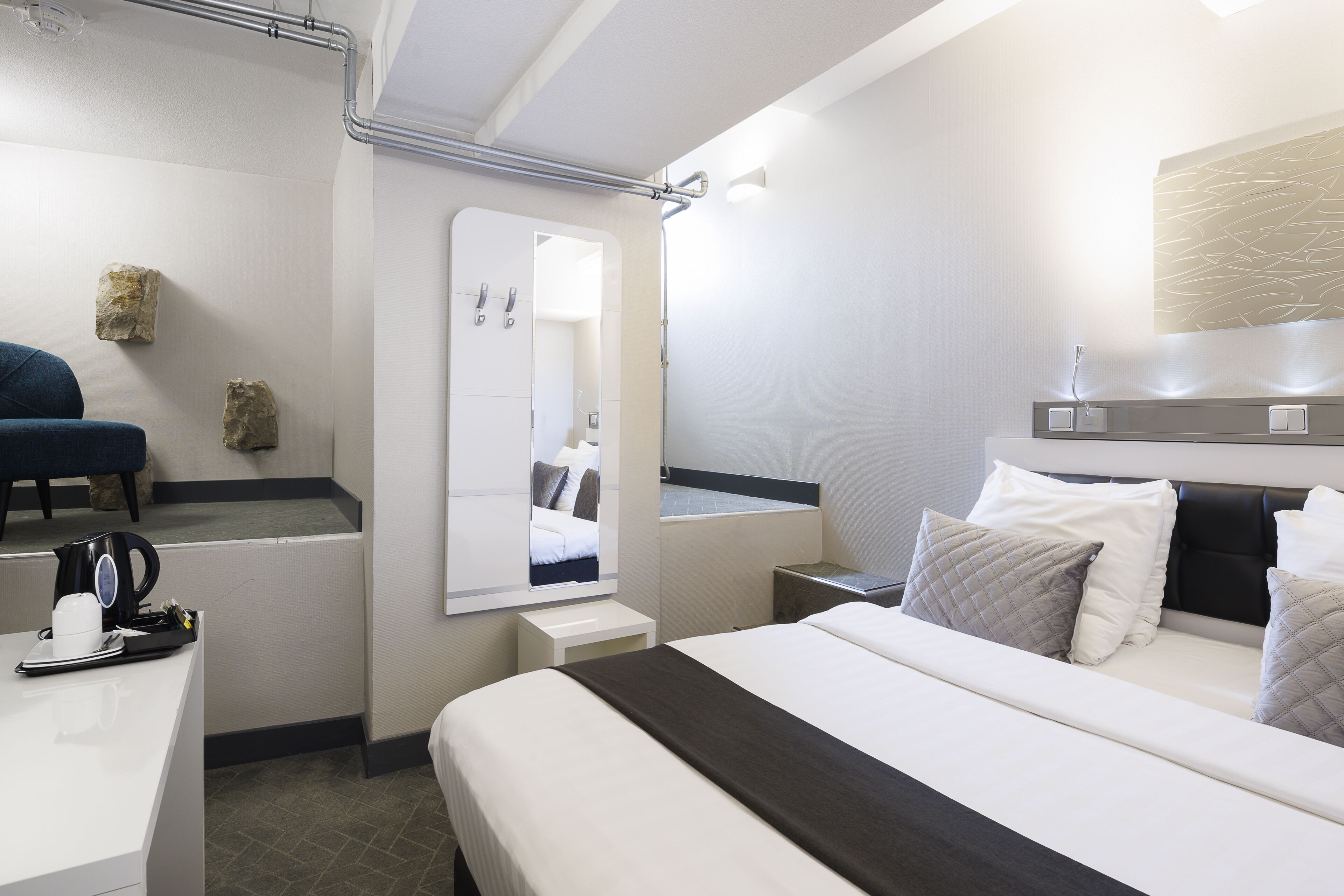 A modern hotel room with a bed, bedside table, and a mirror.