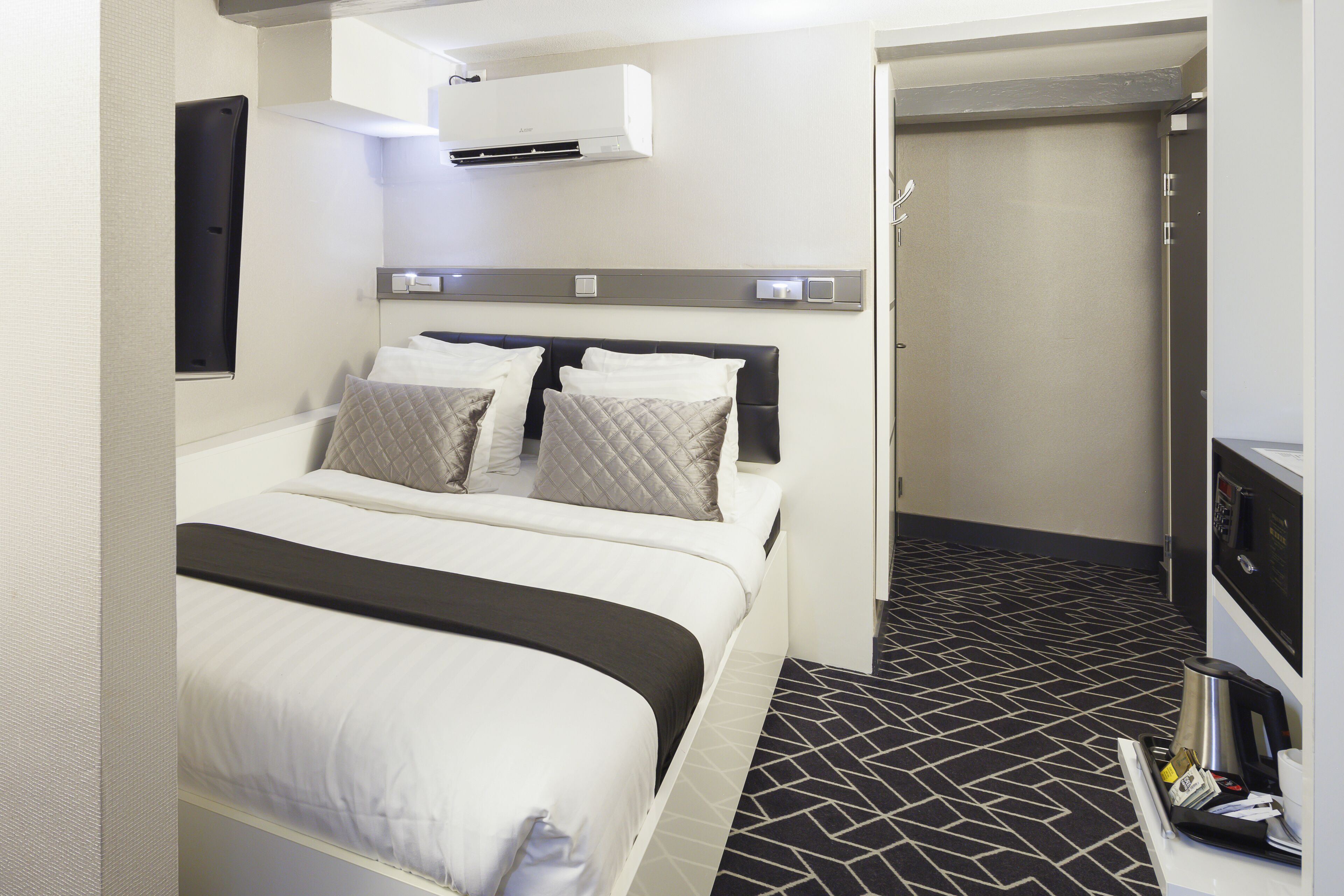Ein Hotelzimmer mit einem Bett, einem Schreibtisch mit Kaffeemaschine und einer Tür zu einem weiteren Raum.