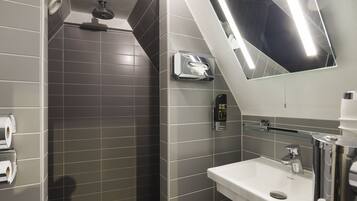A modern bathroom with grey tiles, a white sink, a glass shelf, and a mirror.