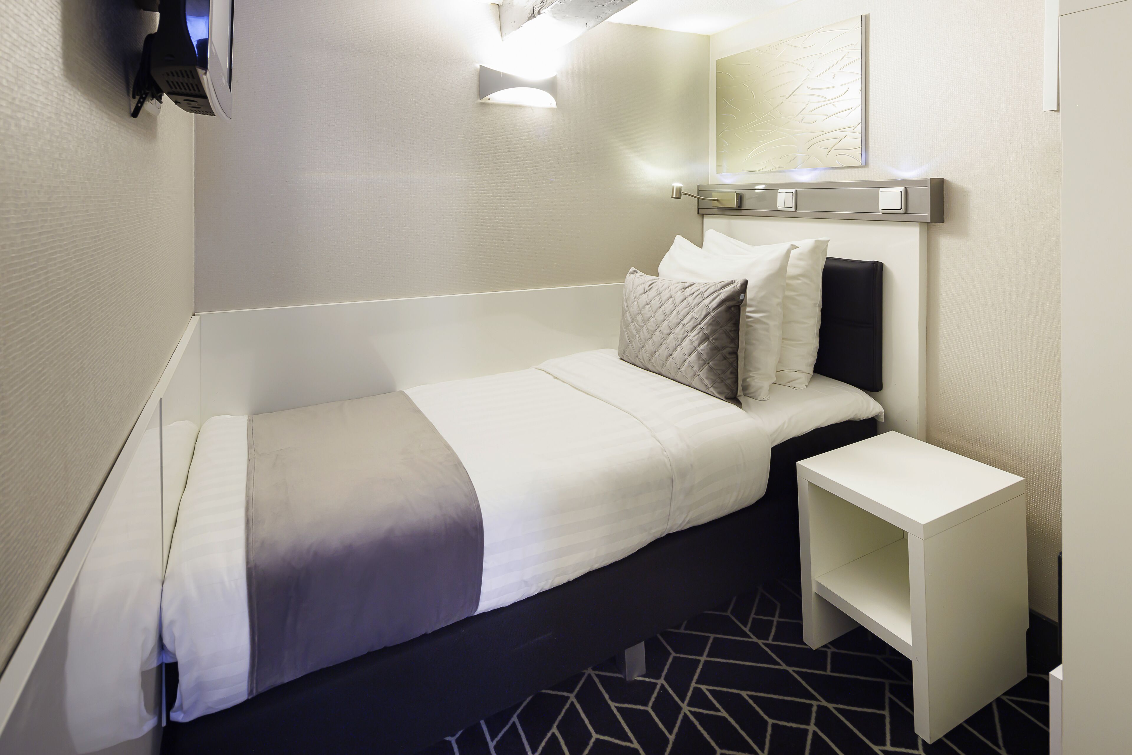 Una moderna camera d'albergo con un letto rifatto, un comodino e una lampada a parete.