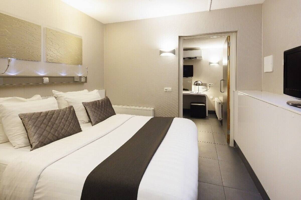 A hotel room with a bed, a desk, a television, and a bathroom visible through an open door.