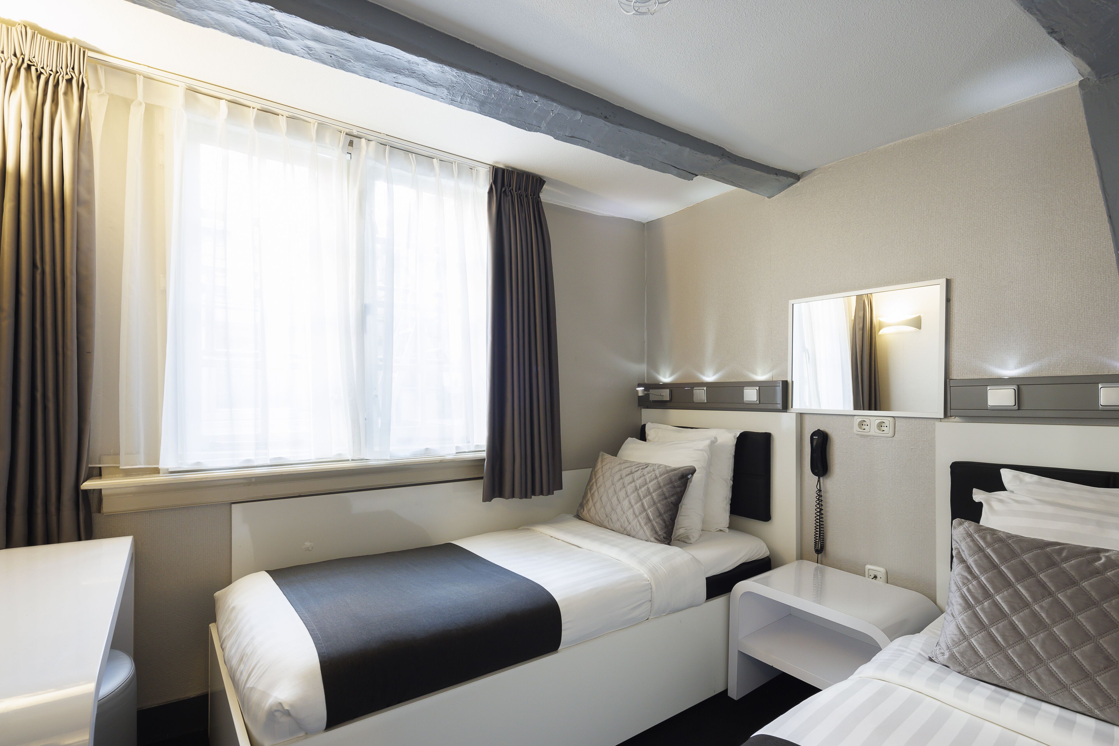 A hotel room with a bed, bedside table, and a mirror.