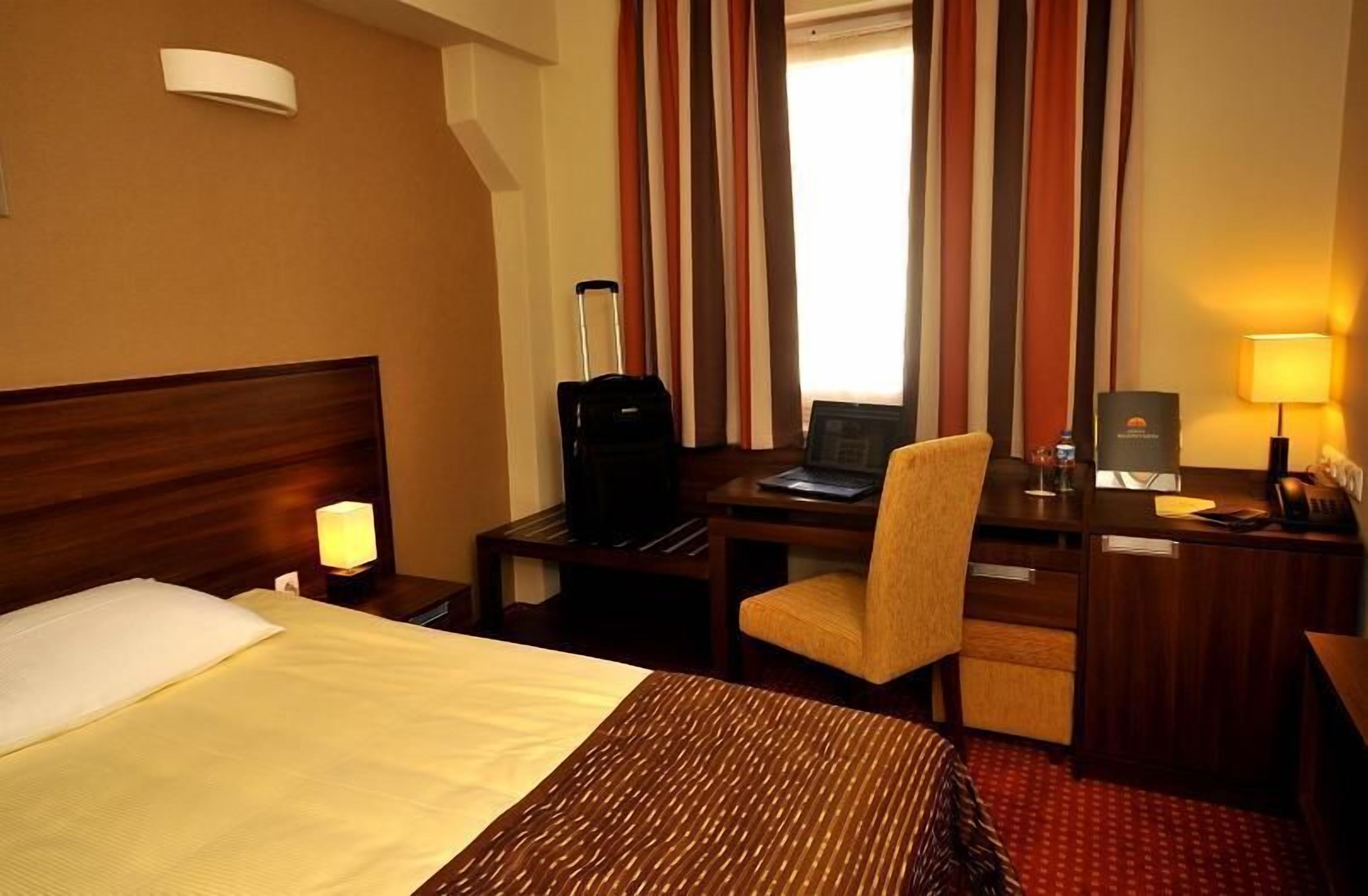 Una camera d'albergo con un letto, una scrivania, una sedia e una valigia.