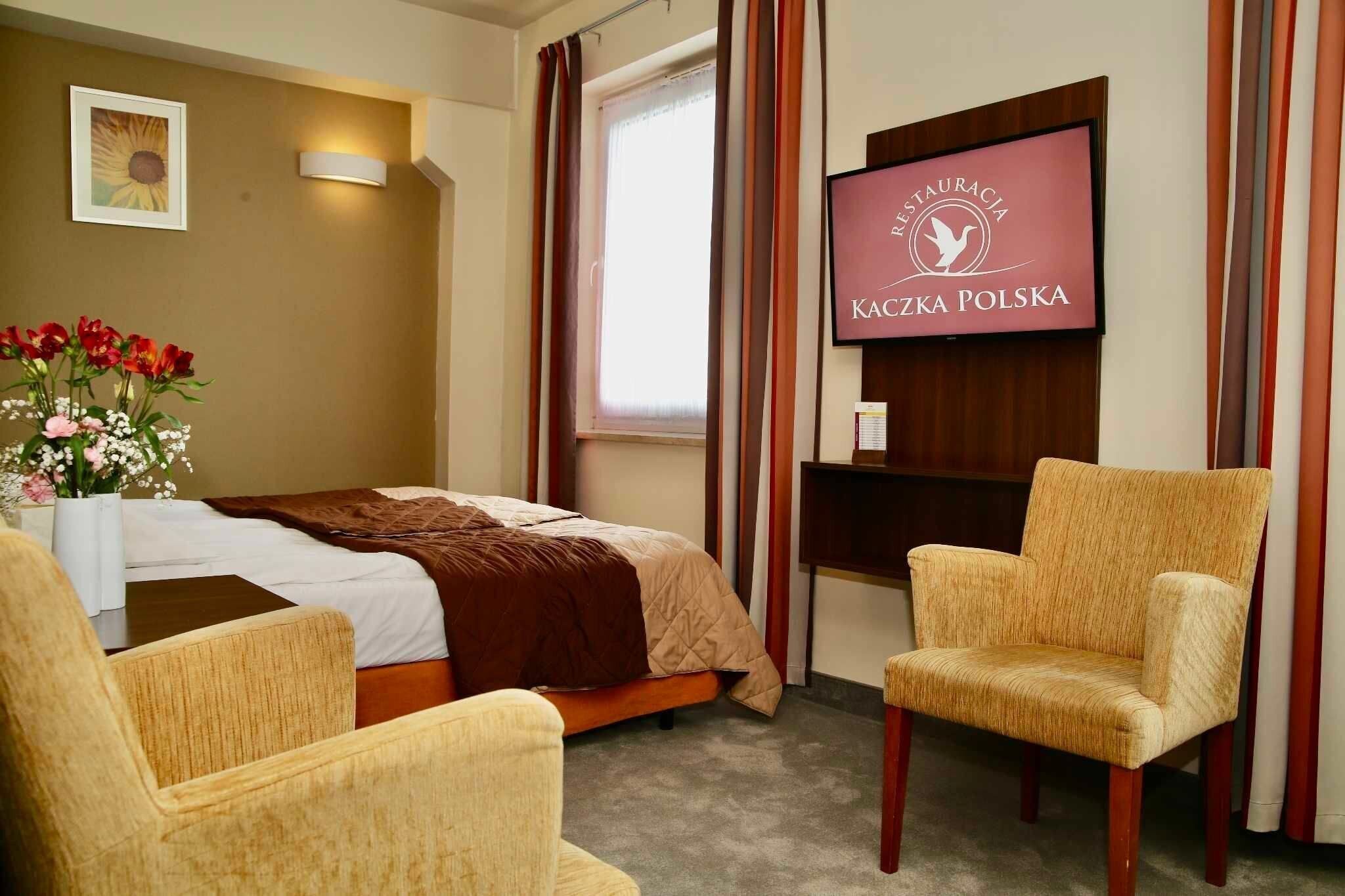 A hotel room with a bed, a TV, a chair, and a flower vase.