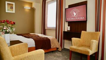 A hotel room with a bed, a TV, a chair, and a flower vase.