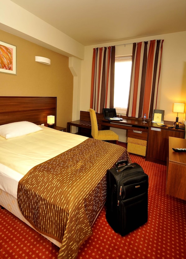 Una habitación de hotel con una cama grande, un escritorio con computadora, una silla y una maleta.