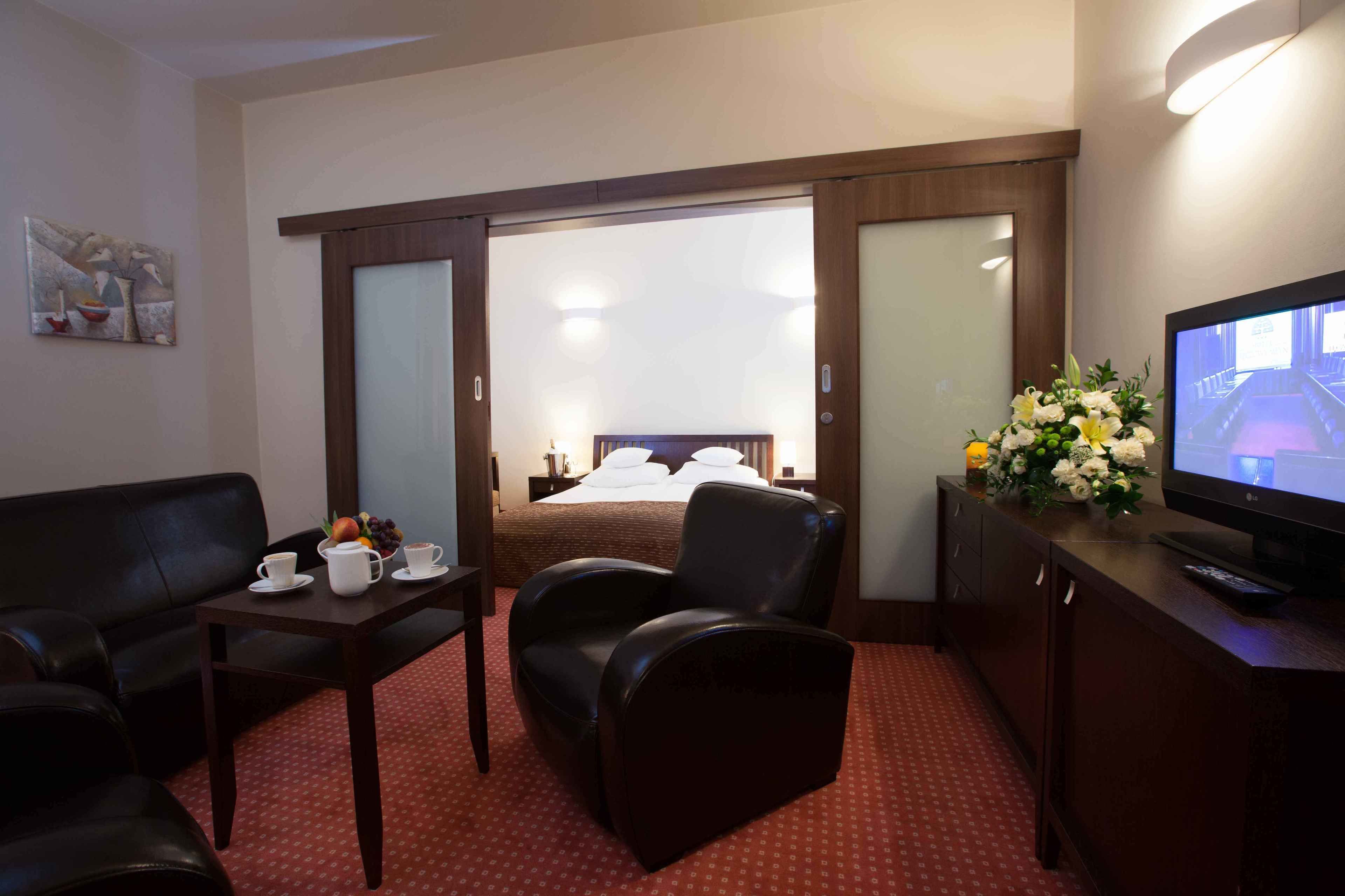 Habitación de hotel con cama, televisión, escritorio y silla, una mesita de centro y un florero.